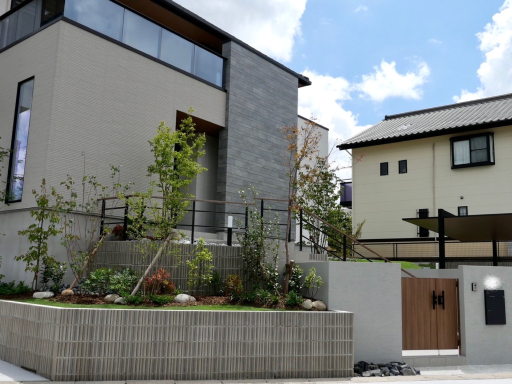 愛知県名古屋市緑区の新築外構工事。アールプランナー（アールギャラリー）住宅。緑化地域の為、植栽や芝生等の緑をふんだんに取り入れ、白の塀やタイルに加え木目調を取り入れてナチュラルな明るい外構に仕上げました。 駐車場にはLIXILのカーポートSCを設置。お庭エリアはウッドデッキと物置・芝生敷きで仕上げました。ファザードデザインに彩りや立体感を持たせるような配置をポイントとした外構デザインです。 ＃ナチュラルモダン　＃施工事例　＃施工実績　＃ミライエエクステリア　＃パートナーホーム　名古屋市名東区・日進店